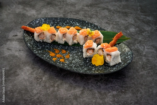 Obraz A plate of sushi with a green leaf on top. The sushi is cut into pieces and has a sauce on it