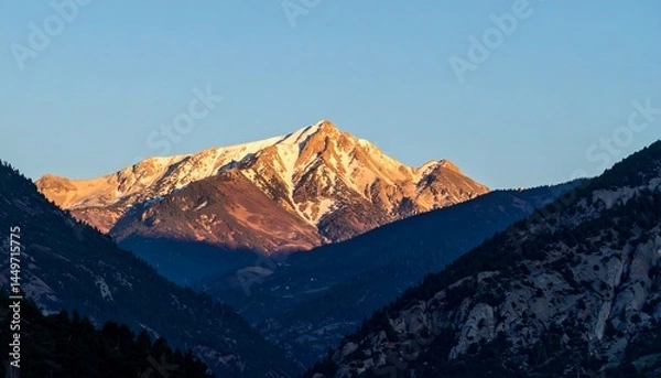 Fototapeta Mountain peak illuminated by sunrise while the valley remains in shadow.