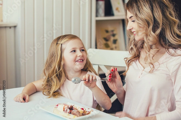 Fototapeta mother and daughter in a cafe sitting at a table and feed each other ice cream.Good relationship of parents and child. Happy moments together.