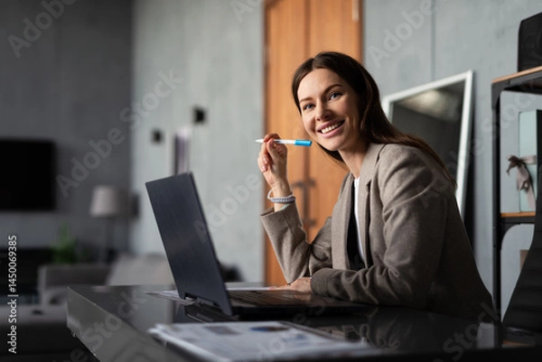 Fototapeta Professional woman working in office. She is seated at desk with a laptop and documents.