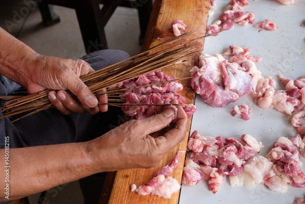 Fototapeta The goat satay seller is skewering slices of goat meat onto the skewers. mutton satay. sate kambing. blurred image. 