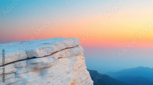 Obraz A rocky cliff edge overlooks distant mountains beneath a colorful sunrise or sunset sky.