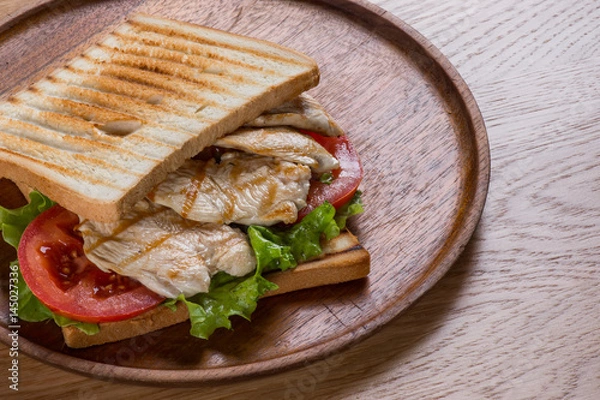 Fototapeta Sandwich with chicken on wooden plate, flat lay top view.
