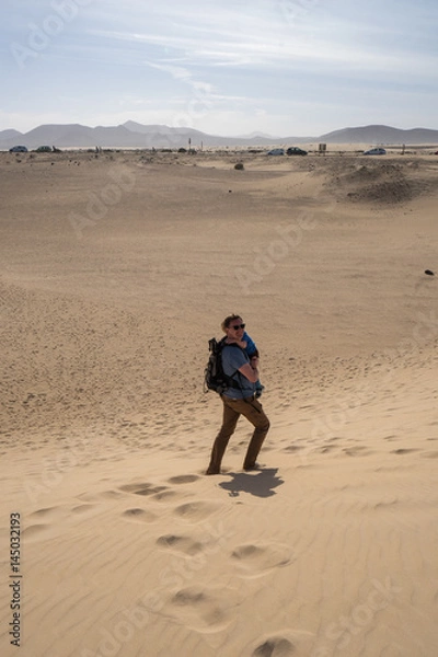 Fototapeta A man with the baby is walking in the sand dunes