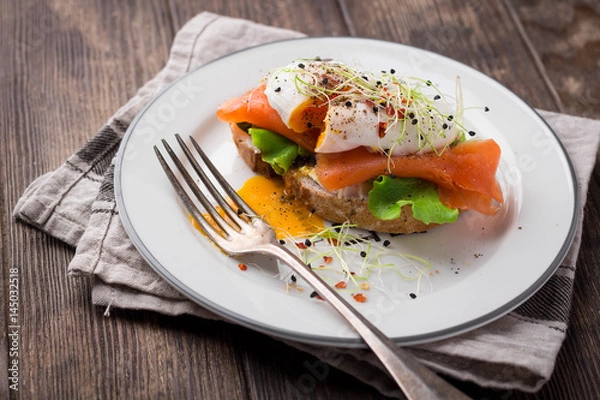 Fototapeta Delicious toast with salad, salted salmon and poached egg on rustic background