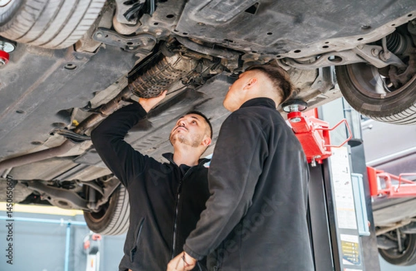Obraz Mechanics inspecting car exhaust system in auto repair shop