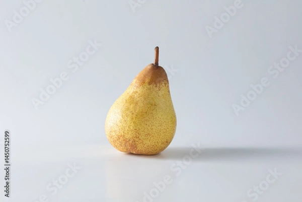 Fototapeta A ripe yellow pear stands alone against a clean white background, captured in soft natural light. This minimalist studio shot highlights its texture and form with elegant simplicity