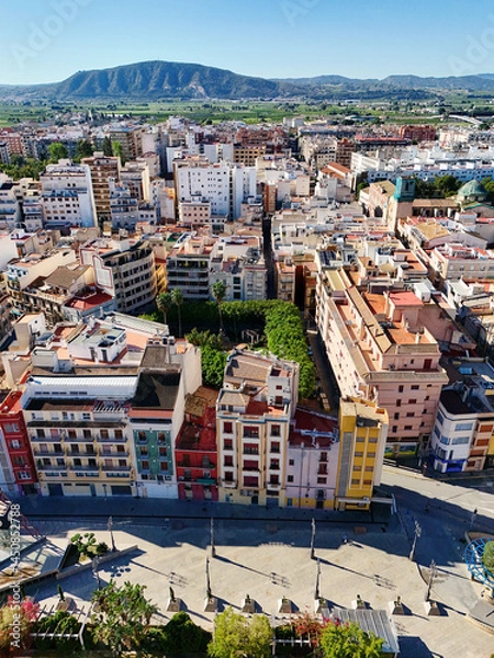 Fototapeta Aerial shot, drone point of view of ancient spanish city of Orihuela with building and mountains and valley with agricultural fields and mountains under clear blue sky during sunny day. Costa Blanca, 