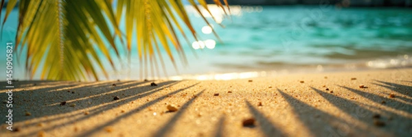 Obraz A serene beach with golden sand and palm tree shadows, turquoise water, and sunlight sparkling on the waves.