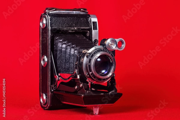 Obraz An old camera, with bellows, folding, portable on a red background.
