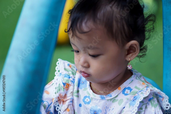 Fototapeta close-up an asian toddler girl plays inside a blue toy car, exploring and enjoying her time at the playground.