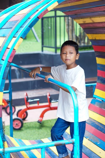 Fototapeta A cheerful asian boy explores a colorful tunnel at the playground, enjoying a fun and active day out.