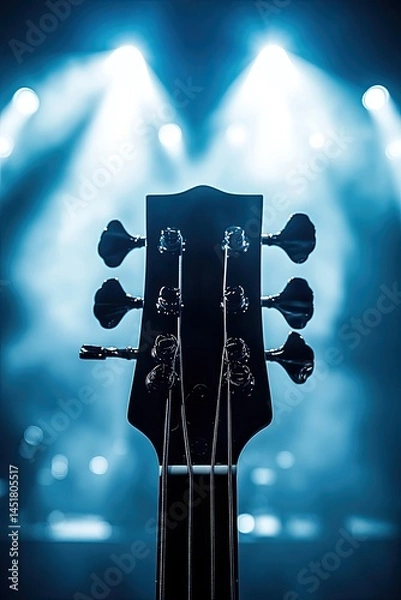 Fototapeta Bass guitar headstock on a stage, illuminated by spotlights.  The headstock is dark, and the background is a blurred, lit stage