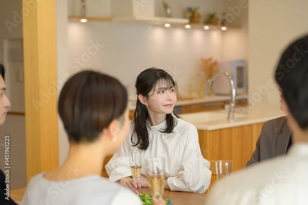 Obraz 若い女性がグラスを片手に周囲と会話を楽しみながら落ち着いた笑顔を見せる瞬間
