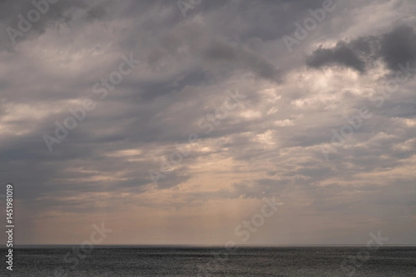 Fototapeta Sun between dark storm clouds over ocean. Dramatic seascape. Clouds and rain flurry over sea.