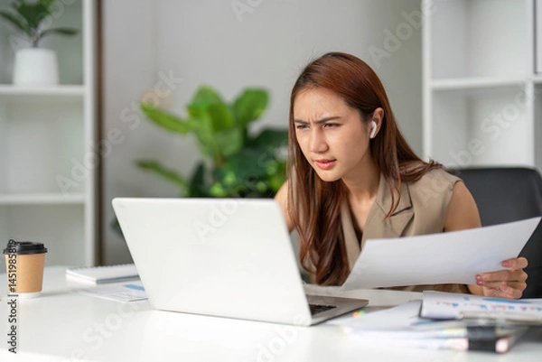 Fototapeta Work Online and Focused Analysis. A young professional shows concentration and determination while analyzing documents at her workstation.