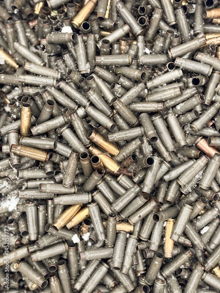 Obraz Wet, snowy, empty cartridge cases for a machinegun, carbine or rifle. Background of shiny cartridges to illustrate armed conflict, war or shooting events. Military background.