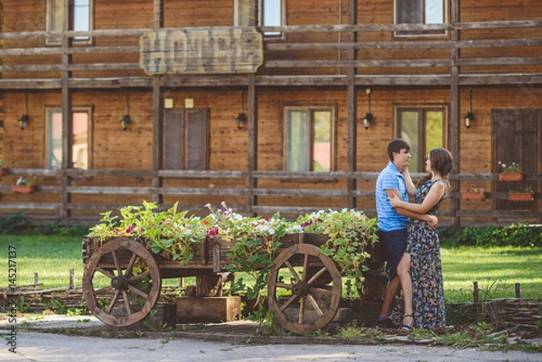 Fototapeta Romantic young couple hugging each other near a decorative wooden carts with flowers, on a background of rustic style.