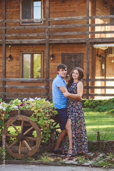 Fototapeta Romantic young couple hugging each other near a decorative wooden carts with flowers, on a background of rustic style.
