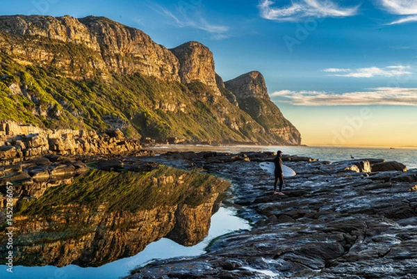 Fototapeta A solo surfer prepares to enter the water - set against a beautiful mountain backdrop at dawn. The tranquil scene embodies communion with nature