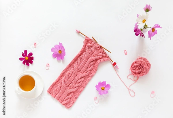Fototapeta Summer craft, needlework. Accessories for hand knitting, cup of green tea, pink cosmos flowers and hand knitted soft pink scarf with unusual braid pattern on white table. Flat lay, copy space, closeup