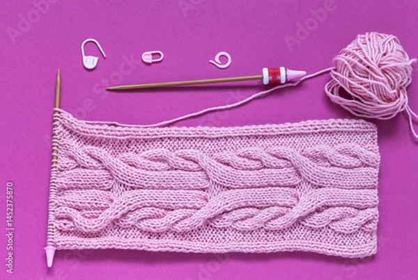 Fototapeta Close-up of accessories for hand knitting on burgundy background. For convenience of knit unusual braid pattern, row counter is put on knitting needle. Pink knitted scarf made of cotton - acrylic yarn