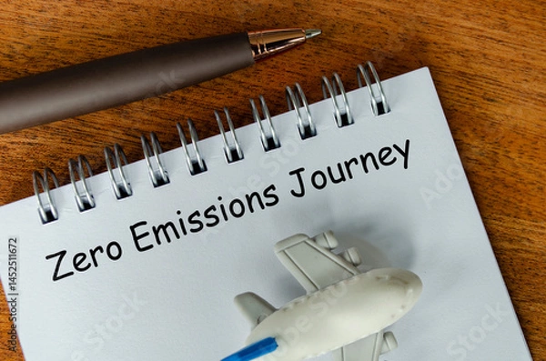 Fototapeta Top view of Zero Emission Journey text on white notepad with small airplane and pen background. Environmental awareness