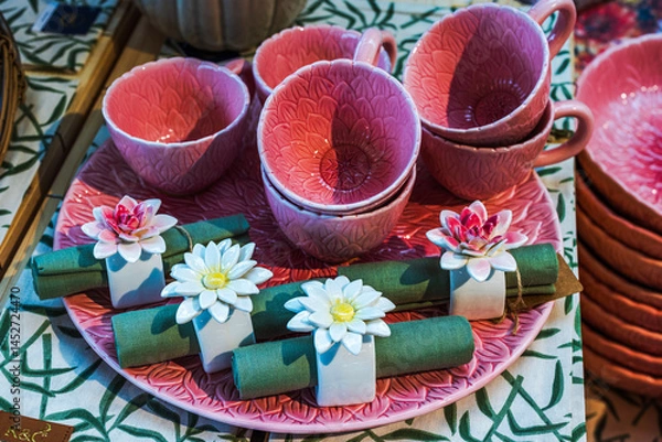 Fototapeta Close up view of pink ceramic cups and plates with floral texture, decorated with napkin holders shaped like water lilies. Sweden.