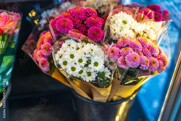 Fototapeta Bouquets of fresh white and pink chrysanthemums wrapped in paper and plastic in flower shop display bucket. Sweden.