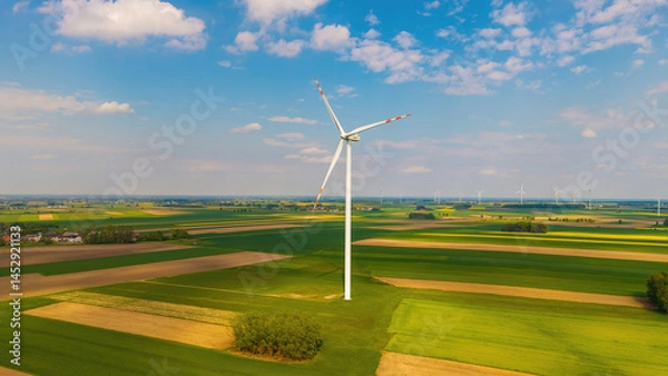 Fototapeta Aerial and drone views of a wind farm and turbines on May Day, surrounded by golden rapeseed fields and lush May greenery, wind energy in a vibrant spring landscape.