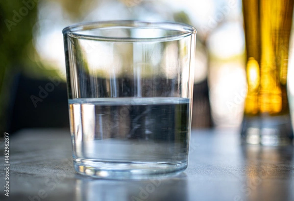 Fototapeta  A half empty or a half full glass of water on a table with nice blurry background.