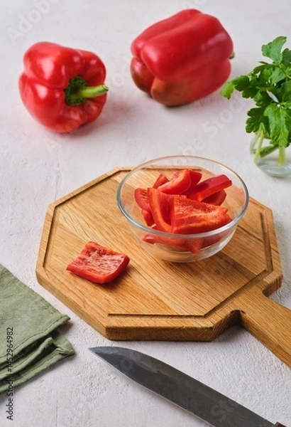 Fototapeta Sweet red pepper cut into squares in a glass bowl on a wooden board on a light concrete background. Ingredients for cooking.