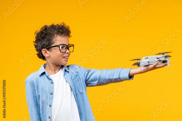 Fototapeta Studio shot of casually dressed African American schoolboy posing over yellow background with generic design drone in his hand, science, technology, modern education concept