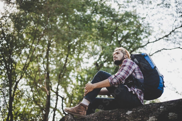 Fototapeta Young hipster man sitting on a tree branch in the park.