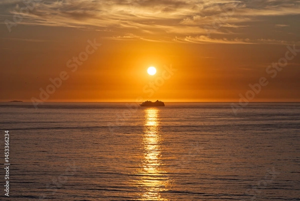 Obraz Cruise ship on the horizon, sunrise with orange sky directly above a ferry boat in the center