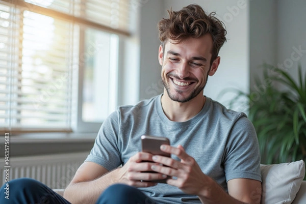 Fototapeta Happy man guy using smartphone at Home, smile and hold phone on he hand with internet technology use of shopping, search, chat, message at inddor living room with beautiful natural light