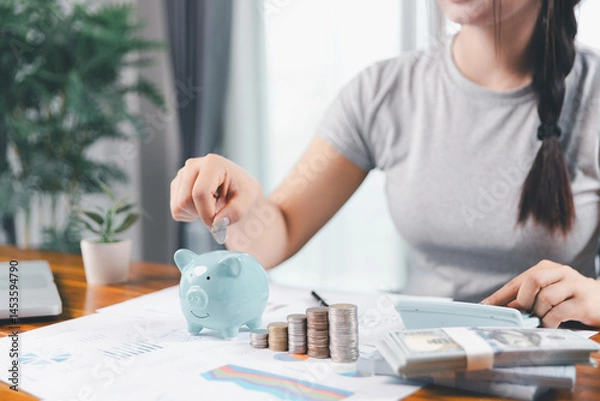 Fototapeta Businesswoman saving money with piggy bank and coins on desk, financial planning and investment concept. Young Asian woman making stack of coin. invest save finance concept, saving money, investment