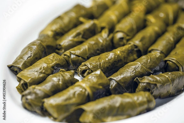 Fototapeta Close-up of tightly rolled, glossy dark green yaprak sarma, a traditional Turkish dish, arranged on a white dish.
