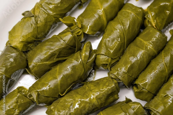 Fototapeta Close-up of tightly rolled, glossy dark green yaprak sarma, a traditional Turkish dish, arranged on a white dish.