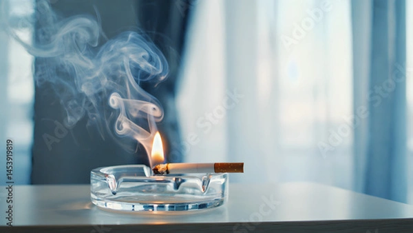 Fototapeta A burning white cigarette with smoke and ash is isolated on a black background, representing the unhealthy habit and danger of tobacco addiction that can cause cancer and death