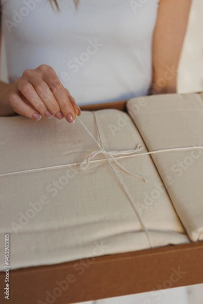 Obraz A woman is carefully tying a small piece of paper with a string, ensuring it is secure and neat for whatever purpose she has in mind