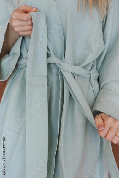 Obraz A woman is currently wearing a light blue robe that has a tie neatly wrapped around her waist, adding a stylish touch to her appearance