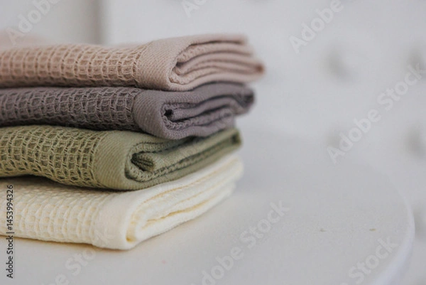 Fototapeta On a table, there are three cozy blankets that are neatly stacked on top of one another, creating a warm and inviting appearance