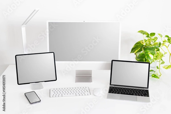 Fototapeta Mockup of different tech gadgets and devices on desk, laptop and desktop computers, tablet and phone