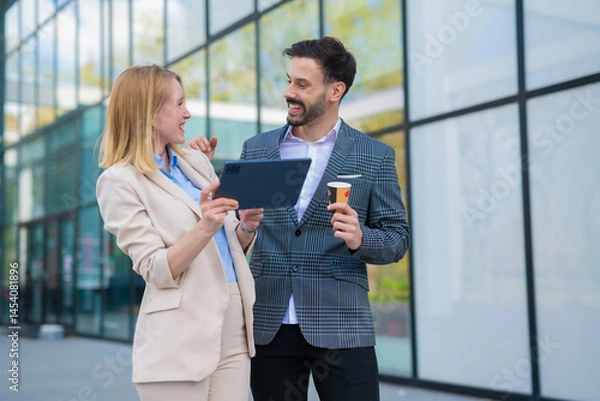 Fototapeta Cheerful business colleagues sharing ideas and laughing while using a digital tablet outdoors during a coffee break.

