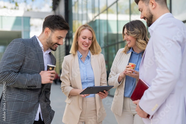 Fototapeta Group of smiling business people having a coffee break and discussing work outside a modern office building.