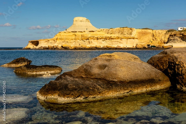 Obraz Dramatic yellow limestone cliffs by the sea in Gozo, Malta. Sunlit limestone cliffs and rocks reflected in clear coastal waters, Gozo, Malta, creating a stunning natural scene.
