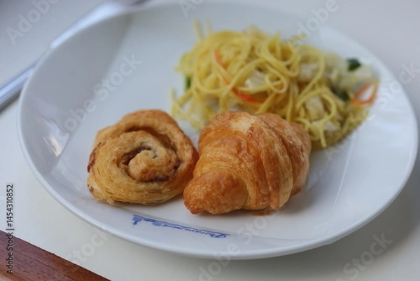Fototapeta A plate of spaghetti and croissant served on a white table.