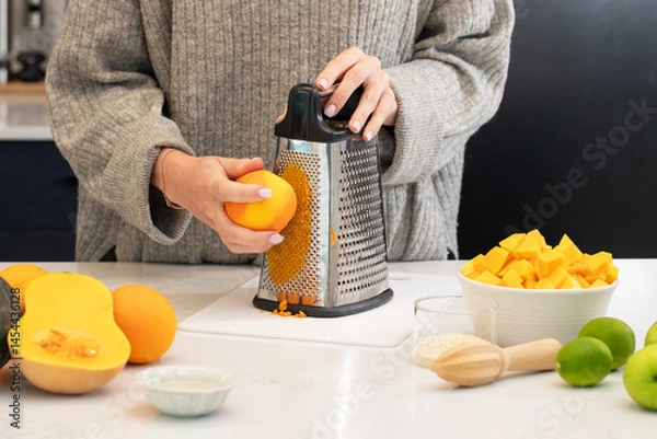 Obraz Caucasian adult grating fresh orange in kitchen with fruit selection for cooking