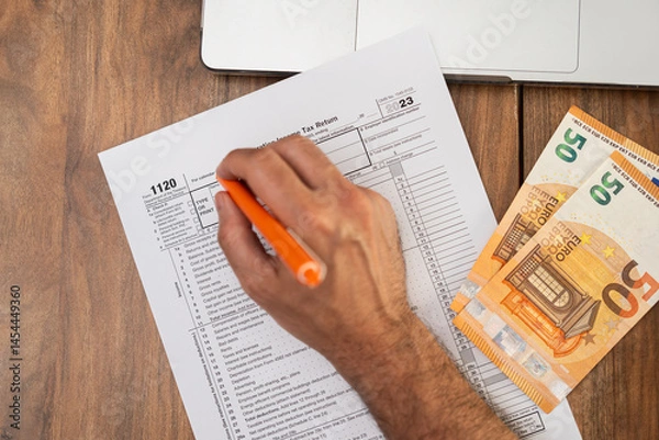 Fototapeta Business owner carefully fills out 1120 tax form on wooden table using laptop and referencing euro bills to ensure all foreign transactions properly recorded